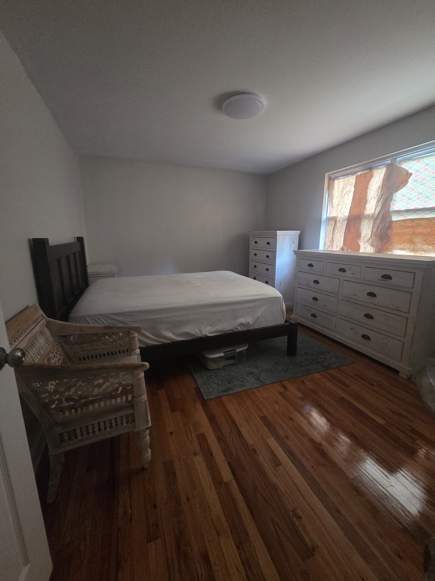 A bedroom with a bed, dressers, and a chair placed in the room.