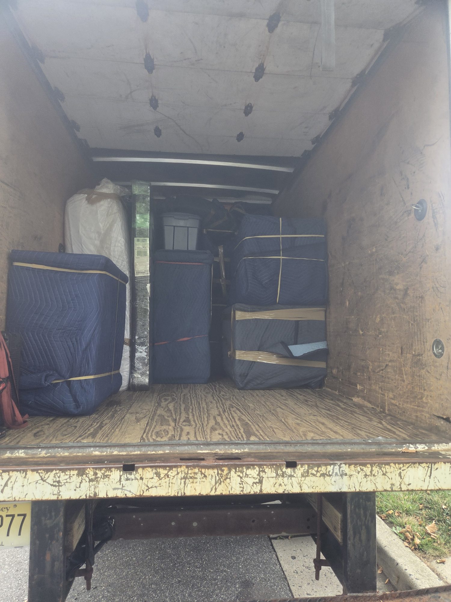 Furniture wrapped in navy moving blankets and secured with straps in the back of a moving truck.