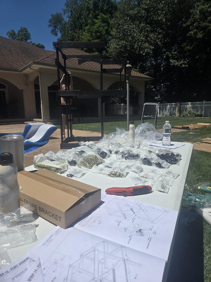 Playset plans and organized hardware in the foreground with the playset frame rising behind them.