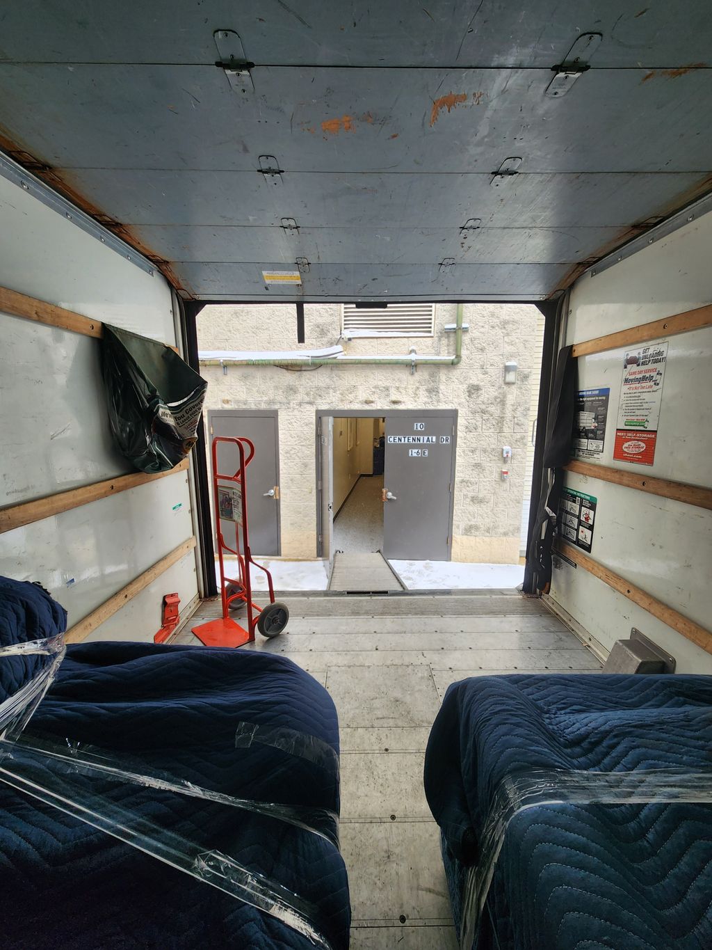A moving truck interior prepared with blankets, straps, and a hand truck.